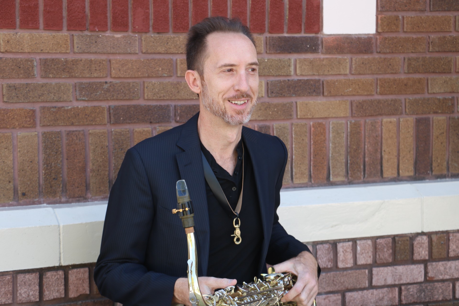 Jaime Hollis professional saxophonist in black blazer holding saxophone